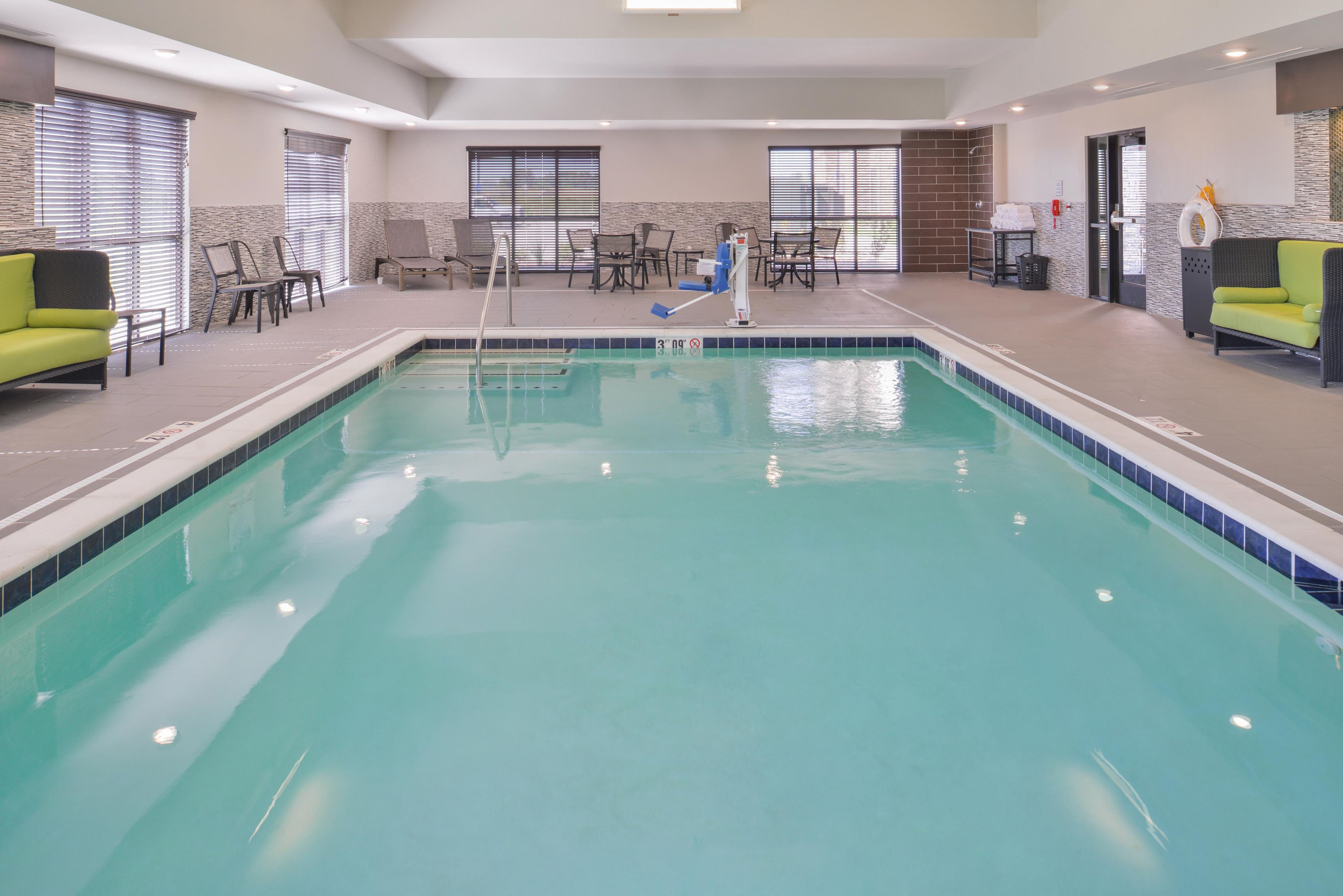 A swimming pool with a diving board, surrounded by chairs and tables.