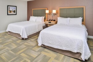 Habitación de hotel con dos camas, una mesita de noche con lámpara y un cuadro en la pared.