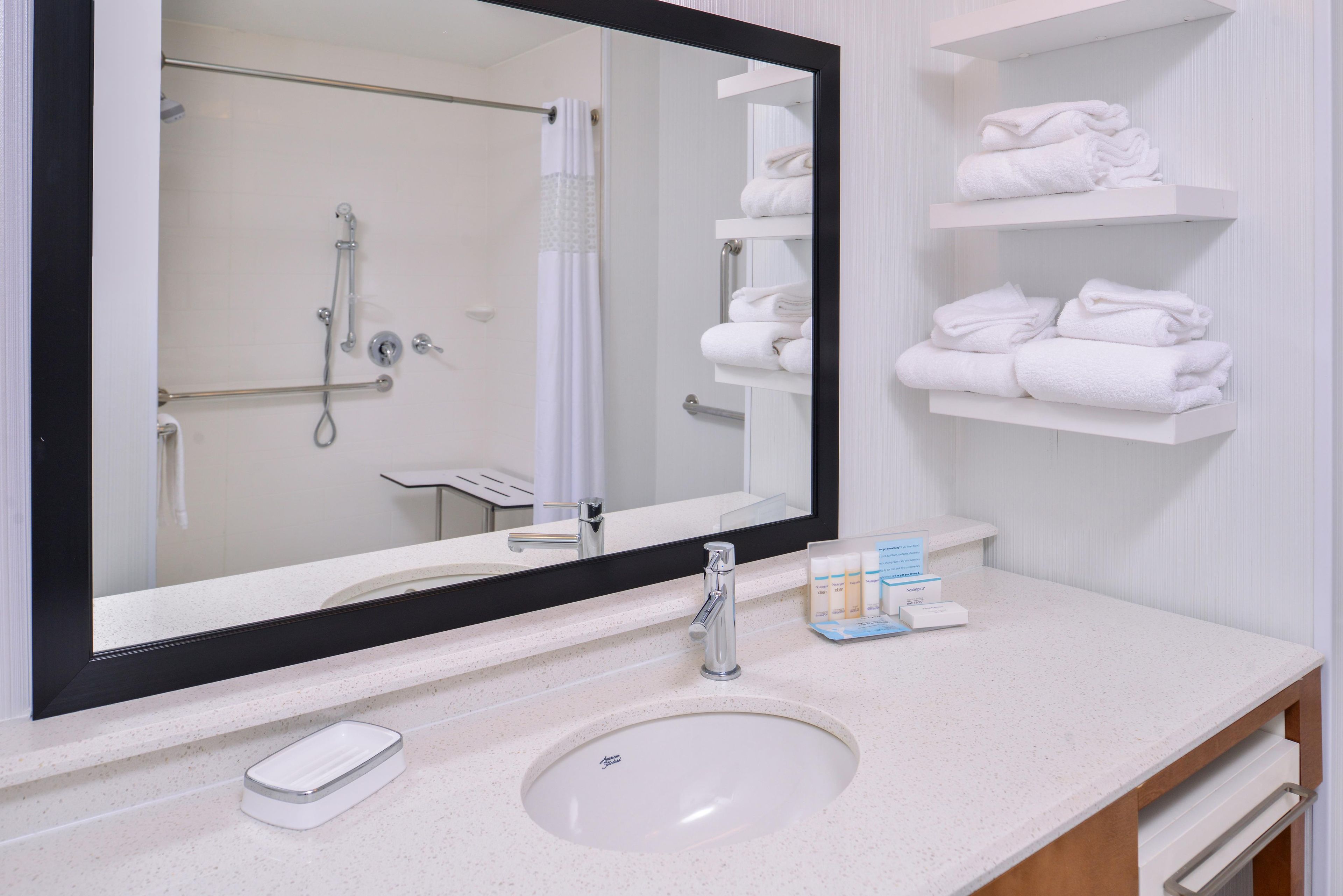 Un bagno con uno specchio grande, un lavandino, un portascopini e uno scaffale con asciugamani piegati.