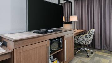 Habitació d'hotel amb televisió de pantalla plana, escriptori amb làmpada, cadira estampada i microones.