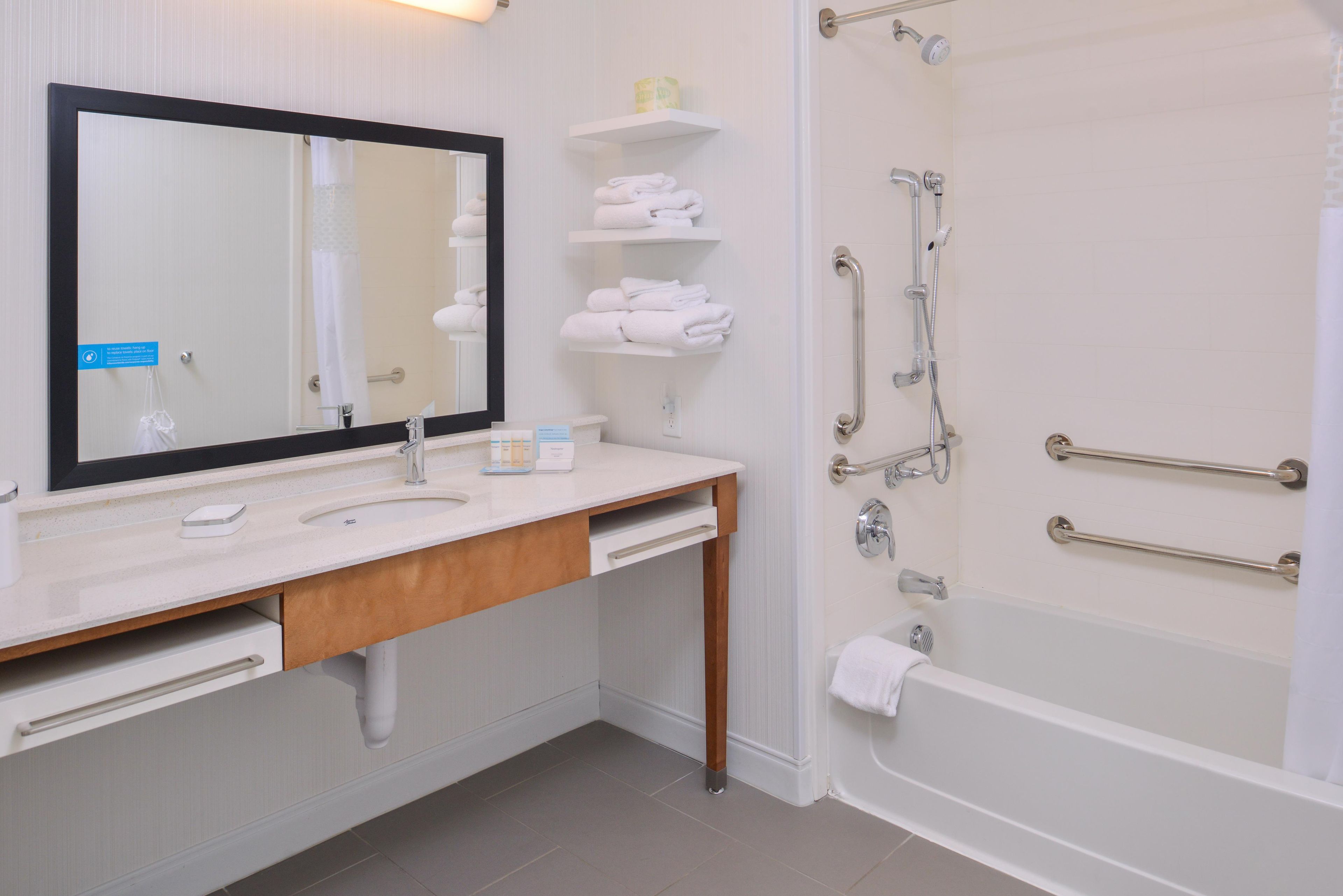 A bathroom with a sink, mirror, towel rack, and a shower with grab bars.