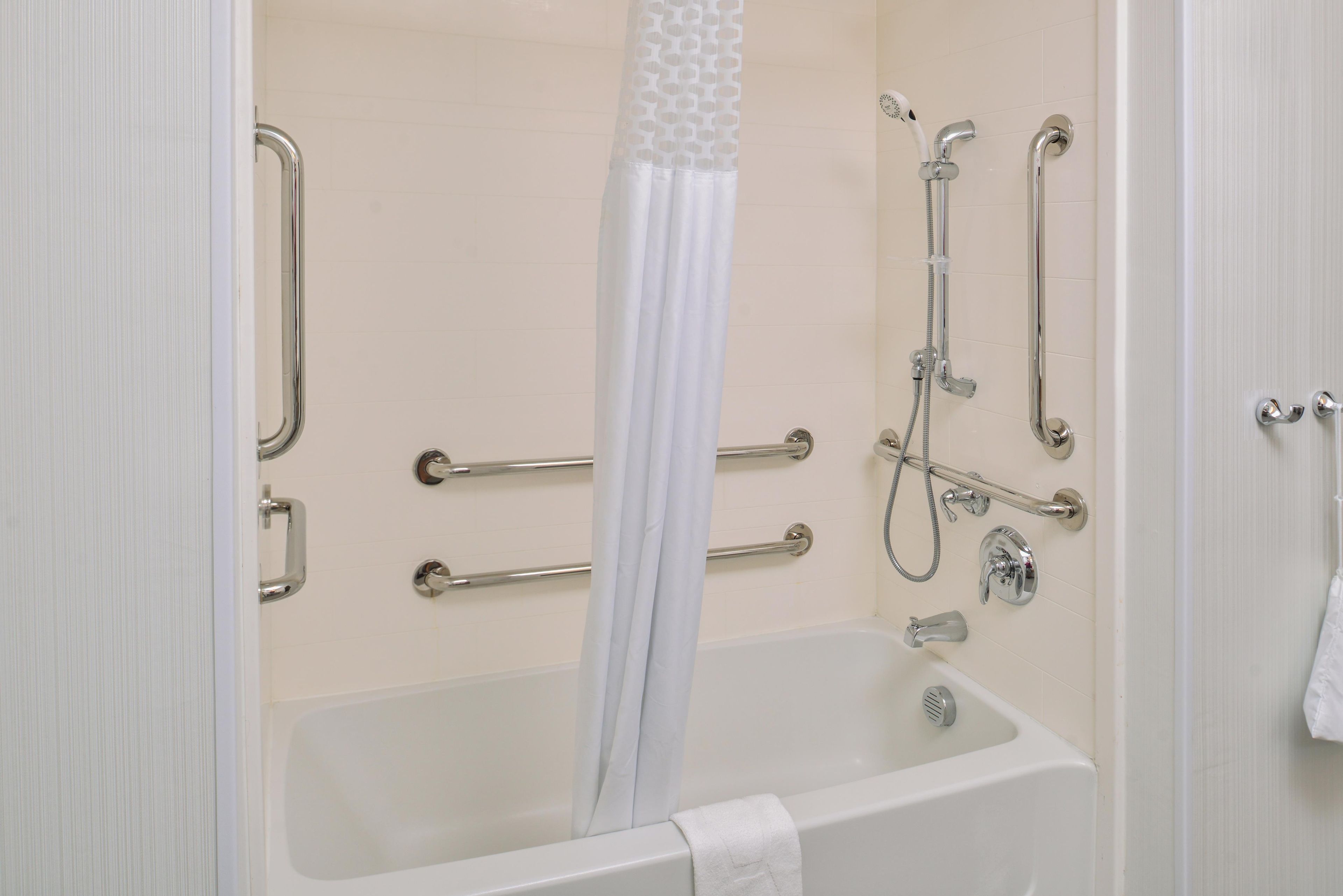 Un baño con bañera, ducha y barras de apoyo.
