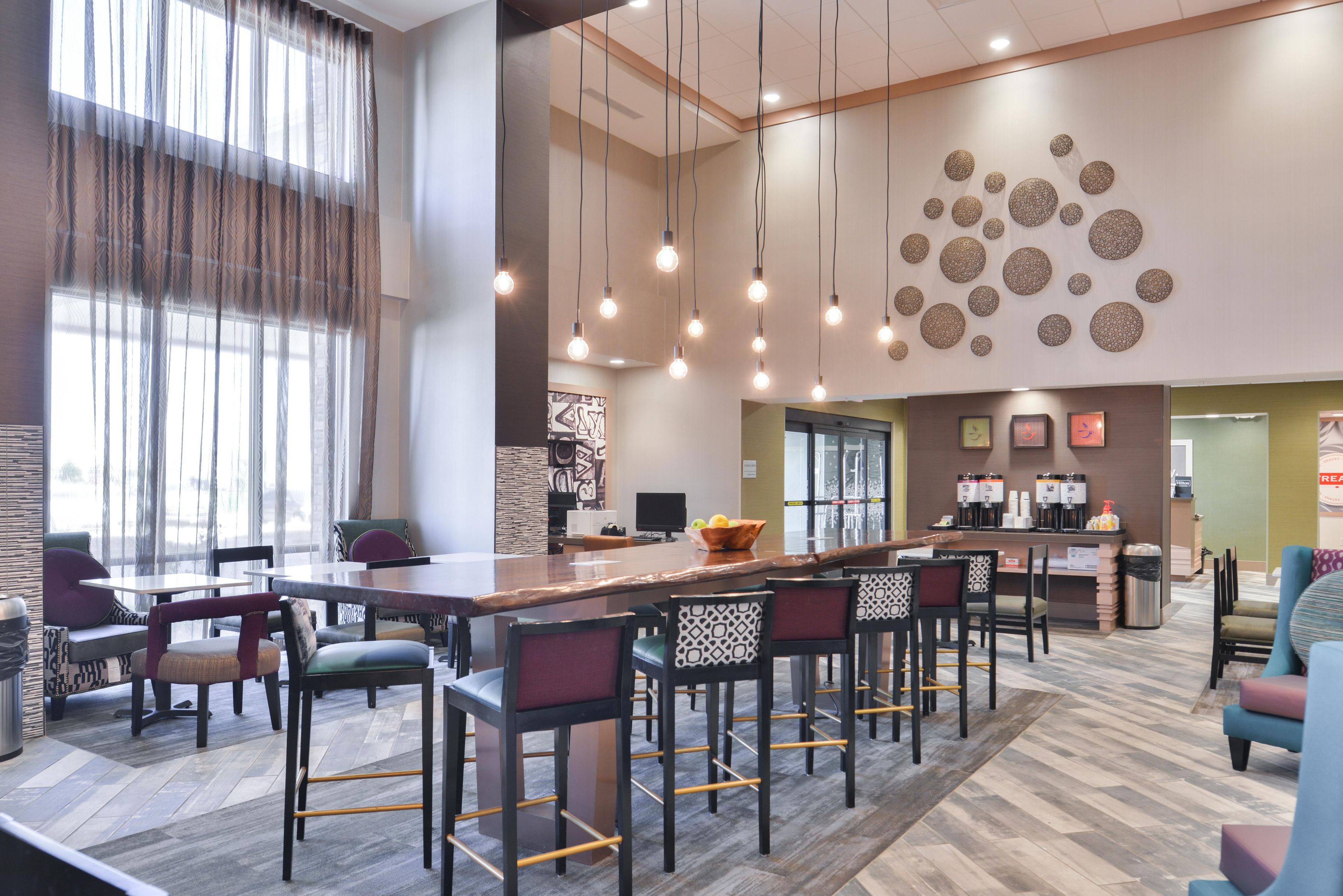 Uma área de bar moderna, com um balcão extenso, vários banquetes e luminárias pendentes.