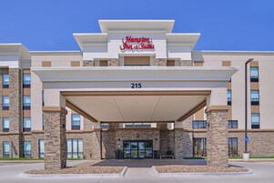 Una entrada de hotel moderna con fachada de piedra, un área de acceso cubierta y cielo despejado.