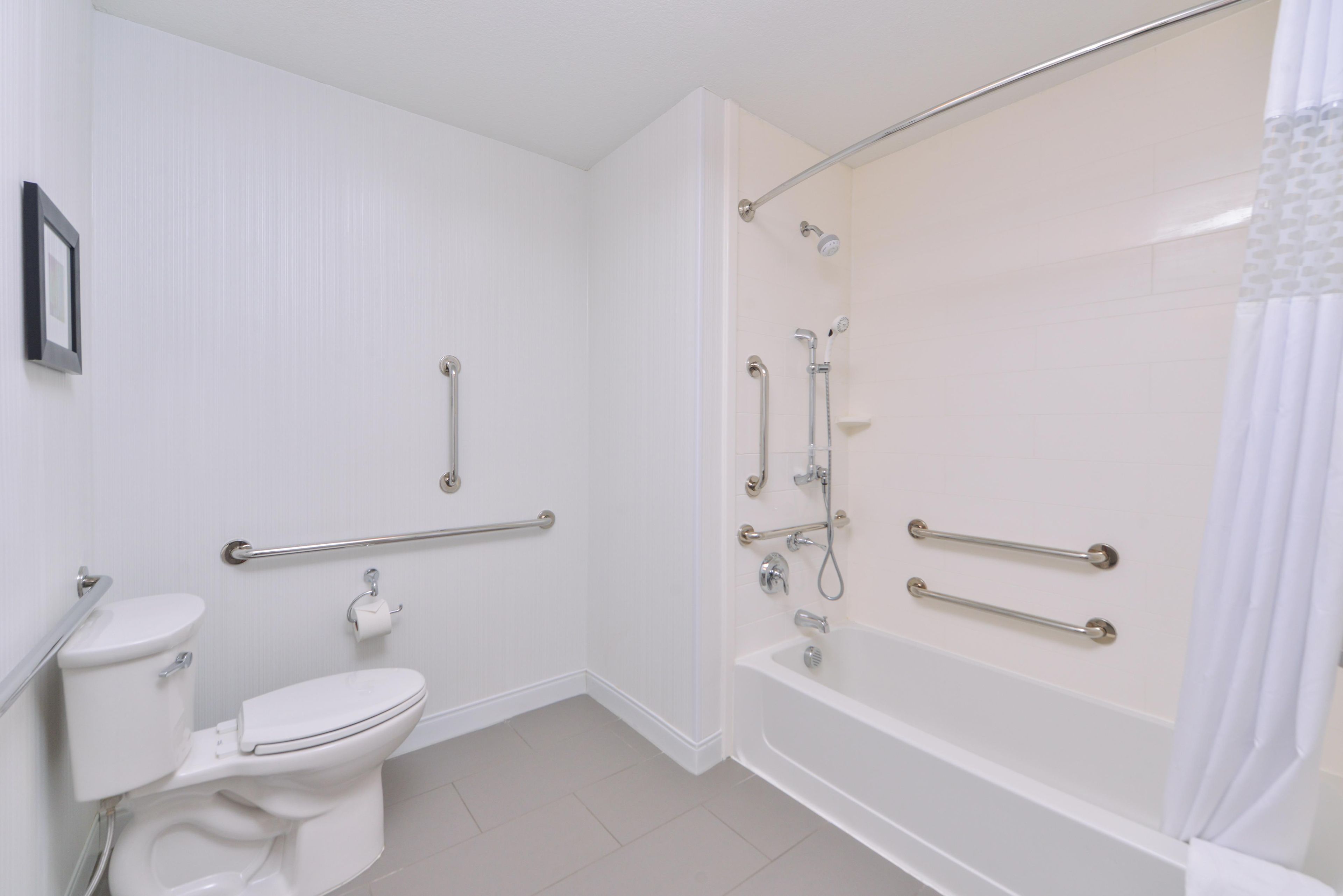 A bathroom with a toilet, a shower, and grab bars.