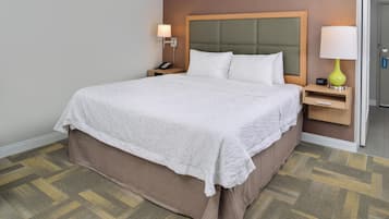 A hotel room with a large bed, a bedside table with a lamp, a phone, and a door to the right.
