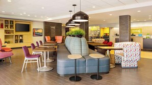 A modern hotel lobby with a seating area, a reception desk, and a dining space.