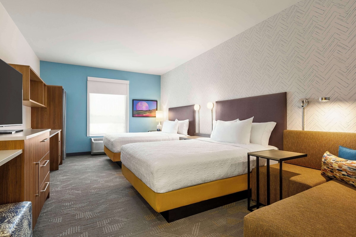 A hotel room with two beds, a desk, a sofa, and a TV.