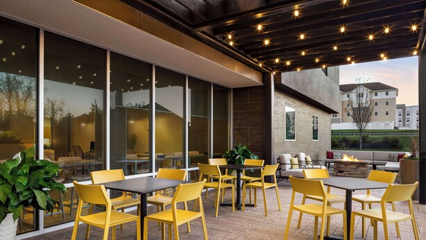 An outdoor patio with yellow chairs and tables, large windows, and a stone fireplace.