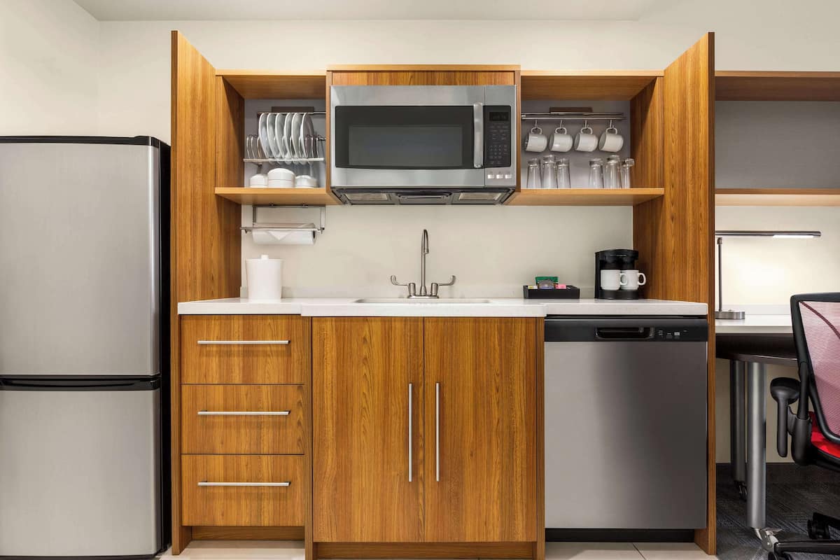 A compact kitchen with wooden cabinets, a stainless steel refrigerator, a microwave, and a dishwasher.