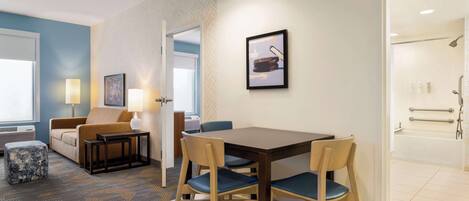 A hotel room with a dining area, a sofa, a coffee table, and a bathroom with a bathtub and shower.