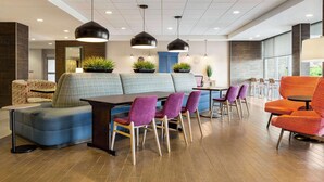 A modern hotel lobby with a seating area, a dining table with chairs, and pendant lighting.