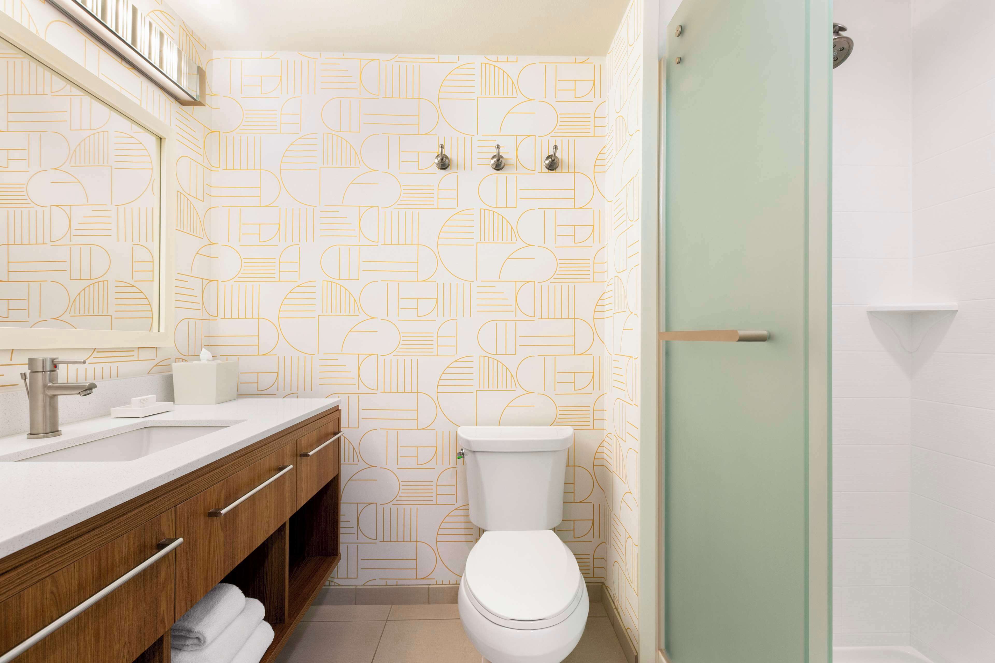 A bathroom with a modern design, featuring a geometric patterned wall, a white toilet, a sink with a silver faucet, and a glass shower enclosure.