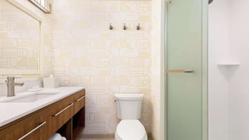 A bathroom with a modern design, featuring a geometric patterned wall, a white toilet, a sink with a silver faucet, and a glass shower enclosure.
