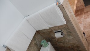 A bathroom with a toilet, a roll of toilet paper, and two white towels hanging on a rack. - Townsman Motel (Boise City)
