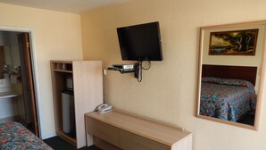 A hotel room with a bed, a desk with a telephone, a TV mounted on the wall, and a painting on the wall. - Townsman Motel (Boise City)