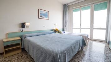 A hotel room with a bed, a nightstand, a telephone, a wall-mounted light, a framed picture, and a window with curtains.
