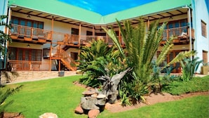 A multi-story building with balconies, a staircase, and a well-maintained garden with palm trees and rocks. - Aan De Bergen Guesthouse South Africa (Swellendam)