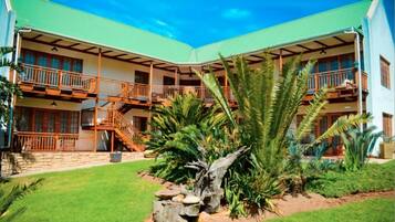 Two-story building with a green roof and balcony on each floor, set amidst a well-mainters lawn with tropical plants.