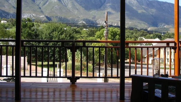 A wooden deck with a metal railing, overlooking a mountainous landscape with greenery and buildings in the distance. - Aan De Bergen Guesthouse South Africa (Swellendam)