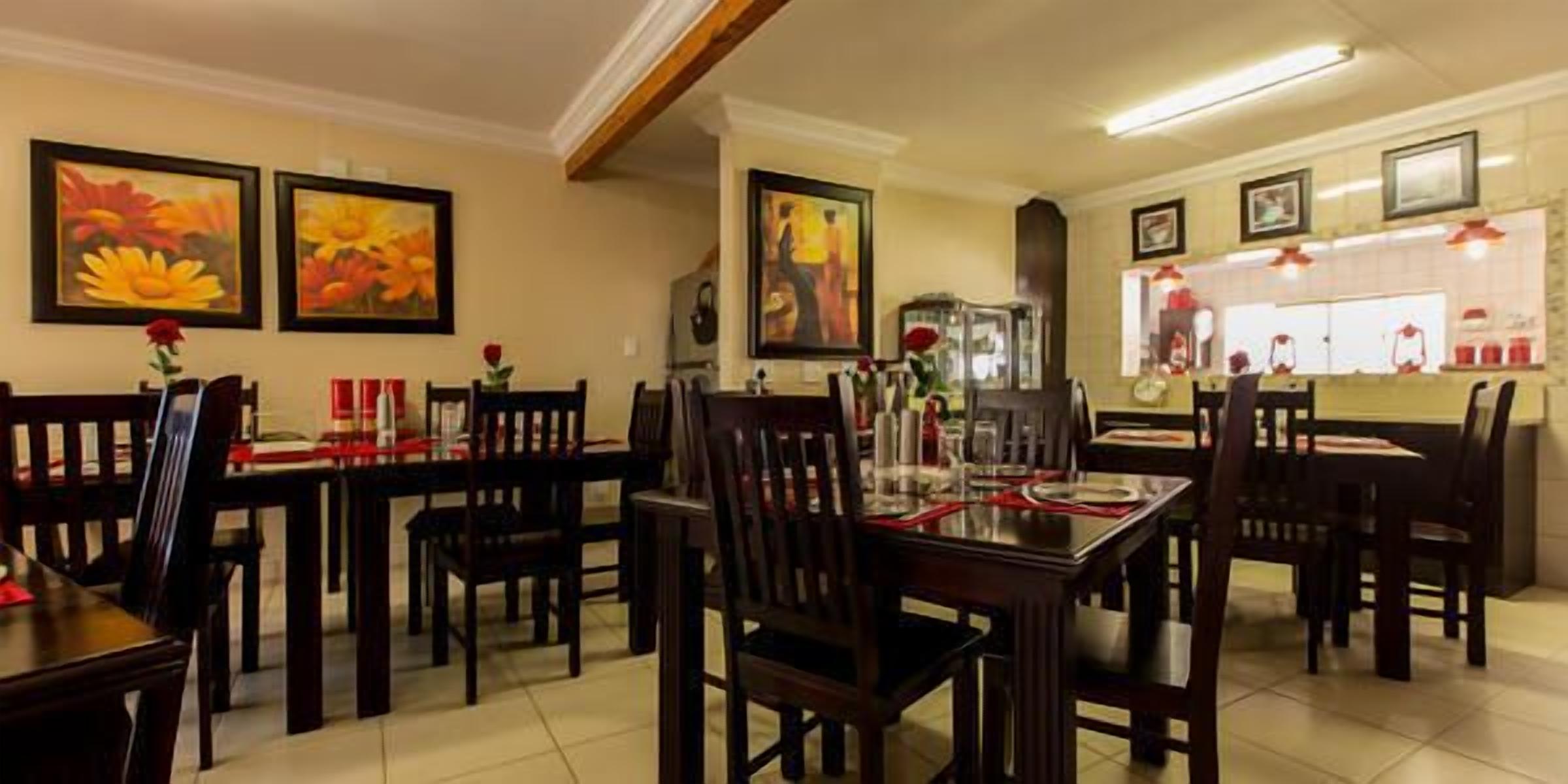 A dining area with wooden tables and chairs, framed artwork on the walls, and a kitchen area visible in the background.