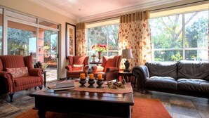A spacious living room with a large window, a fireplace, and a leather sofa. - Home Guesthouse (Rustenburg)