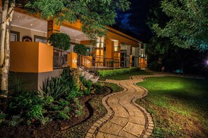 A hotel with a curved pathway leading to a gated entrance, surrounded by lush greenery and a well-maintained lawn. - Home Guesthouse (Rustenburg)