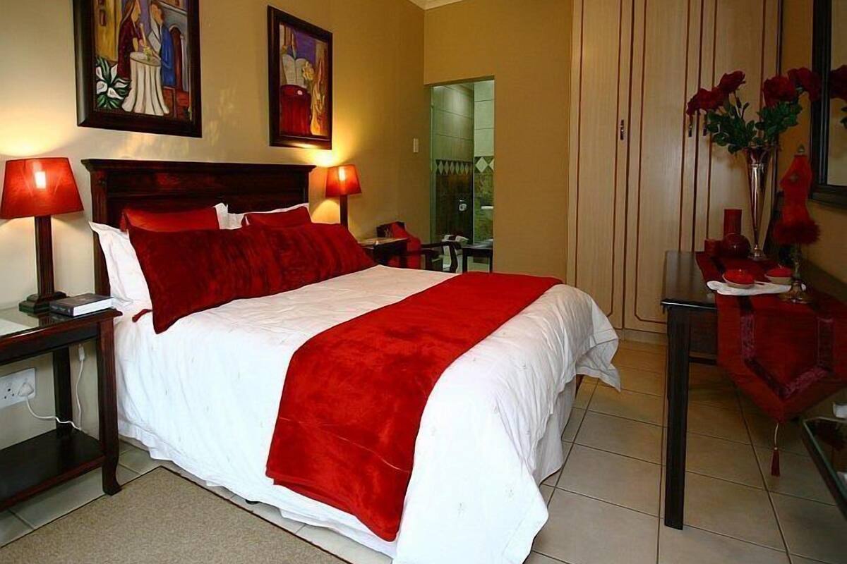 Una camera d'albergo con un letto grande, due lampade ai piedi del letto, un comodino, una scrivania con una sedia, uno specchio e un armadio.