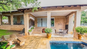 A brick house with a pool, patio furniture, and potted plants. - Home Guesthouse (Rustenburg)