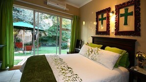 A bedroom with a large bed, green curtains, and a view of the outdoors through a sliding glass door. - Home Guesthouse (Rustenburg)