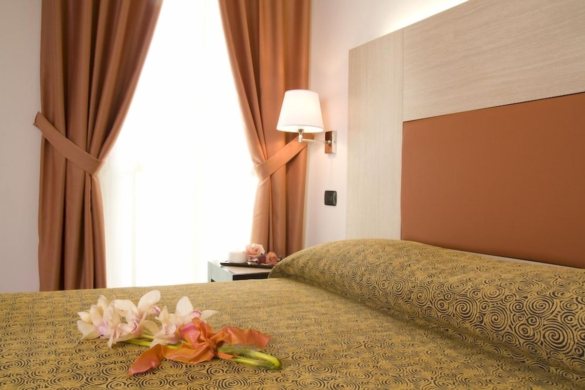 A hotel room with a bed, a nightstand, a lamp, and curtains.