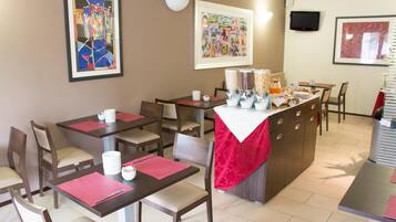 A dining area with multiple tables and chairs, a buffet counter with food items, and artwork on the walls.