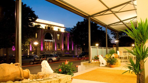 A covered outdoor area with a stone wall, potted plants, and a large planter with a statue. - Hotel Fontanelle (Bertinoro)
