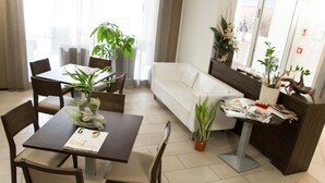 A modern living room with a dining area, featuring a sofa, a coffee table, and several chairs. There are potted plants and a magazine on the table. - Hotel Fontanelle (Bertinoro)