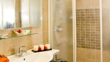 A bathroom with a glass shower enclosure, a sink with a mirror, and a glass shelf with toiletries.