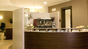 A modern hotel lobby with a curved reception desk, a seating area with a striped rug, and a coffee machine. - Hotel Fontanelle (Bertinoro)