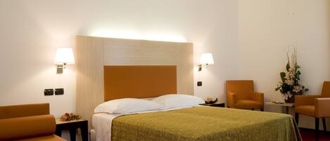 A hotel room with a large bed, two armchairs, a small table, and a nightstand.