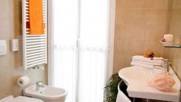Een badkamer met toilet, bidet, wastafel en een handdoekrek met een oranje handdoek.