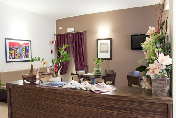 Un área de recepción con mostrador de madera, obras de arte enmarcadas, un televisor y un arreglo floral.