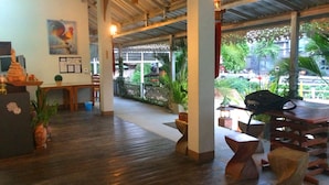 A spacious indoor area with wooden flooring, a dining area with tables and chairs, and a view of the outdoors through large windows. - The Heart of Pai Resort (Pai)