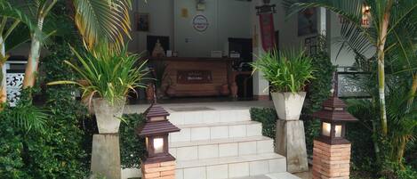 Entrada de hotel con diseño tradicional, que presenta un letrero acogedor, una escalera que conduce al vestíbulo y plantas en macetas.
