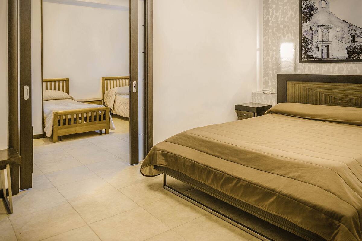 Habitación de hotel con una cama grande, dos camas más pequeñas, una mesita de noche y un teléfono instalado en la pared.