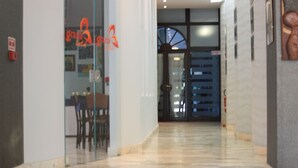 Um saguão de hotel com parede de vidro, balcão de recepção e porta que dá para outra área.