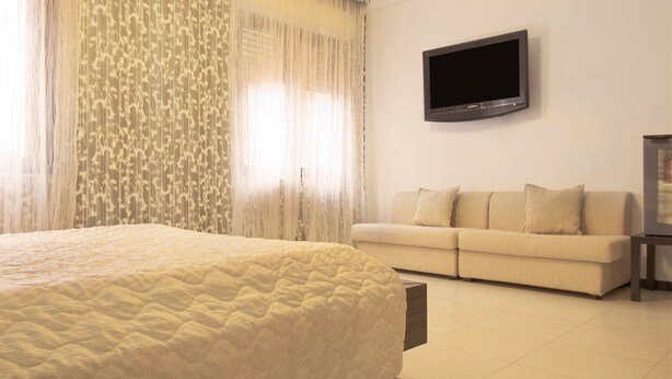 Una habitación de hotel con cama, sofá, televisión montada en la pared y ventana con cortinas.