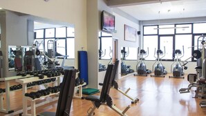 Ginásio com máquinas de cardio, pesos livres e espelho grande.