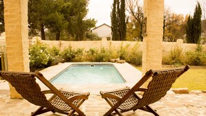 A pool area with two wooden lounge chairs facing the pool, surrounded by stone walls and greenery. - The Ibis Lounge (Nieu-Bethesda)