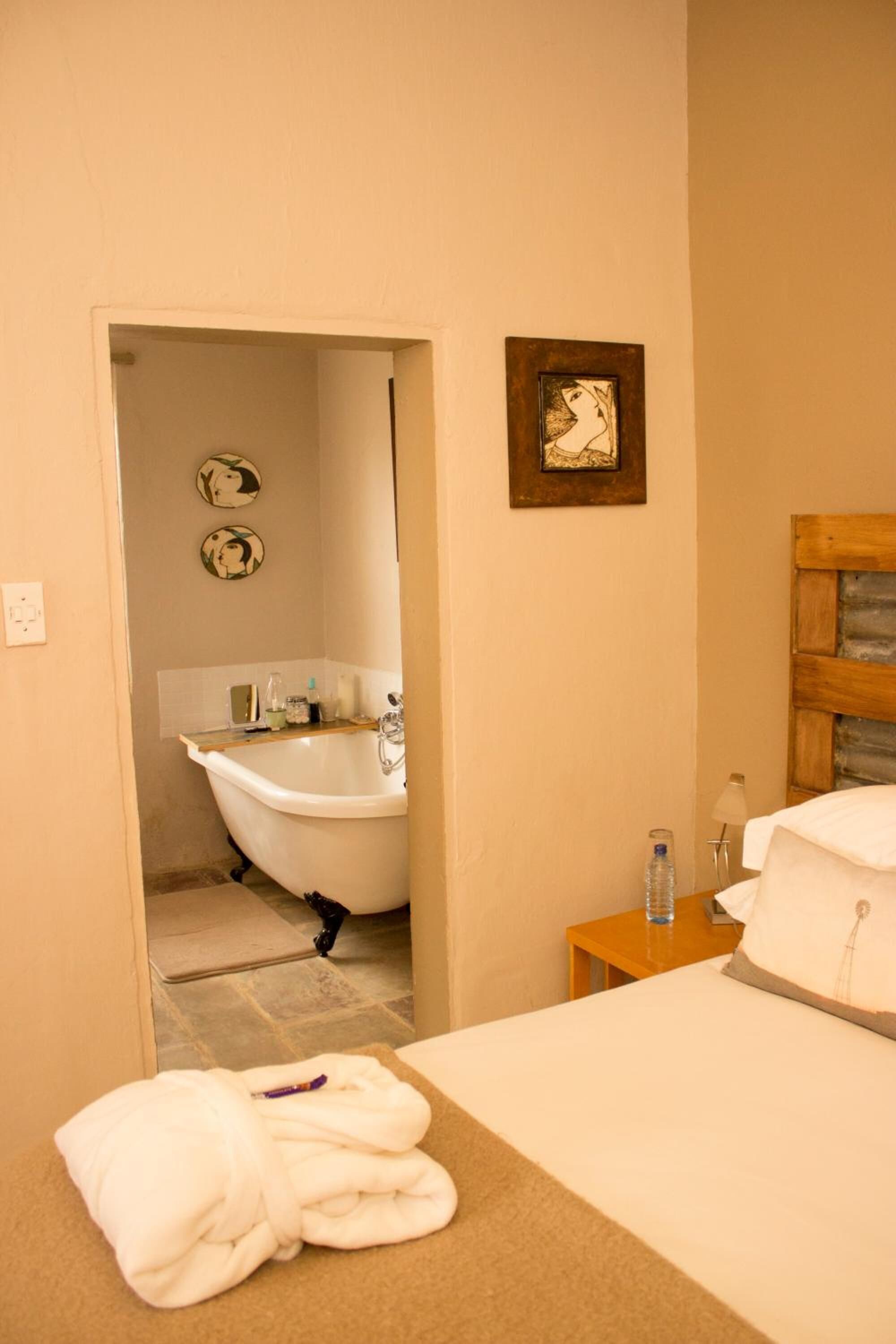 Habitación de hotel con bañera, cabecera de madera, mesita de noche con botella de agua y una toalla sobre la cama.