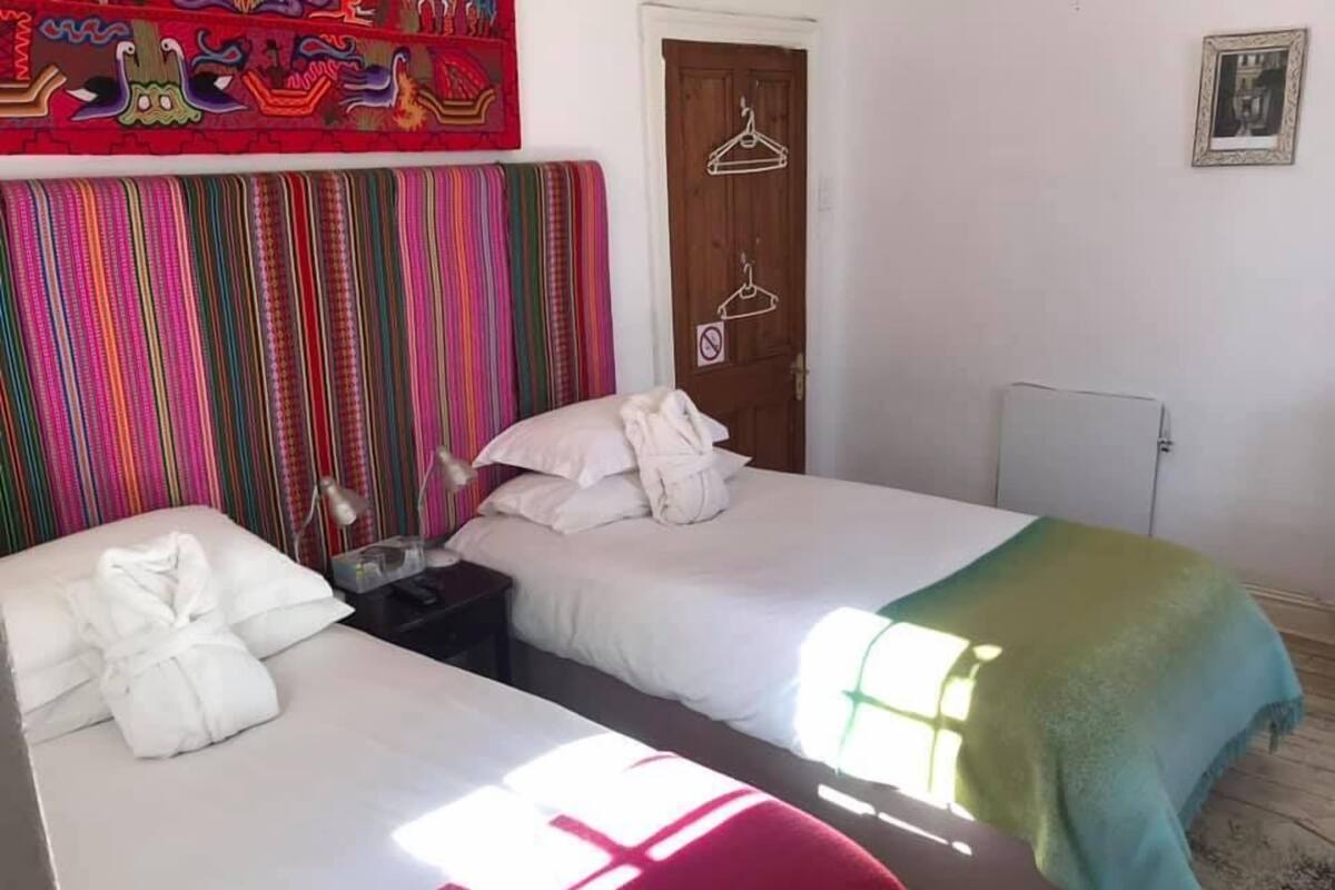 Ein Hotelzimmer mit zwei Betten, einem farbenfrohen, gestreiften Vorhang, einer Holztür und einem gerahmten Bild an der Wand.