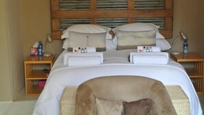 A neatly made bed with white linens and a wooden headboard. There are two bedside tables, each with a lamp and a bottle of water. - The Ibis Lounge (Nieu-Bethesda)