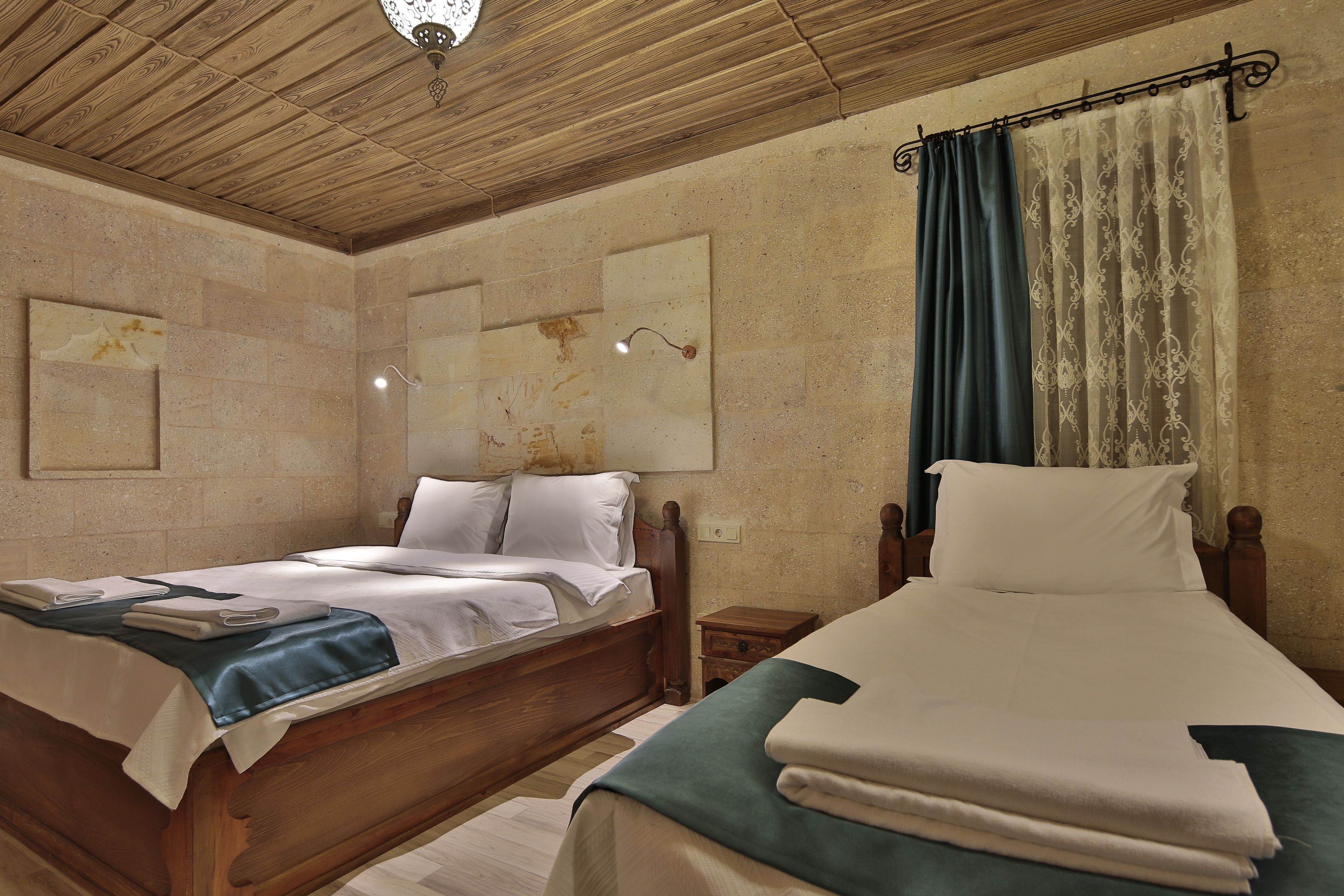 Camera da letto con due letti, testiere in legno, soffitto in legno e un lampadario a parete.